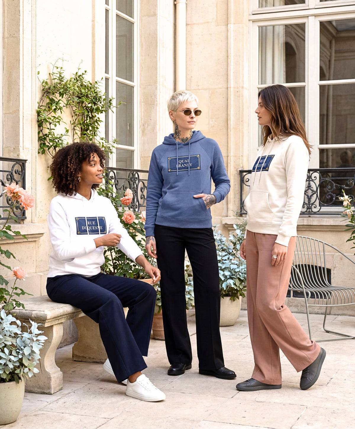 Trois femmes portant des hoodies Salut Fred blanc, écru et bleu ardoise de la collection Rues de France dans une cour parisienne lumineuse