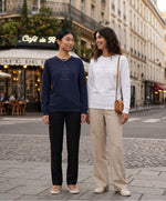 Deux femmes portant des sweatshirts Salut Fred « Tu baises dans mon estime. », l’une en bleu marine et l’autre en blanc, dans une rue parisienne devant un café parisien classique
