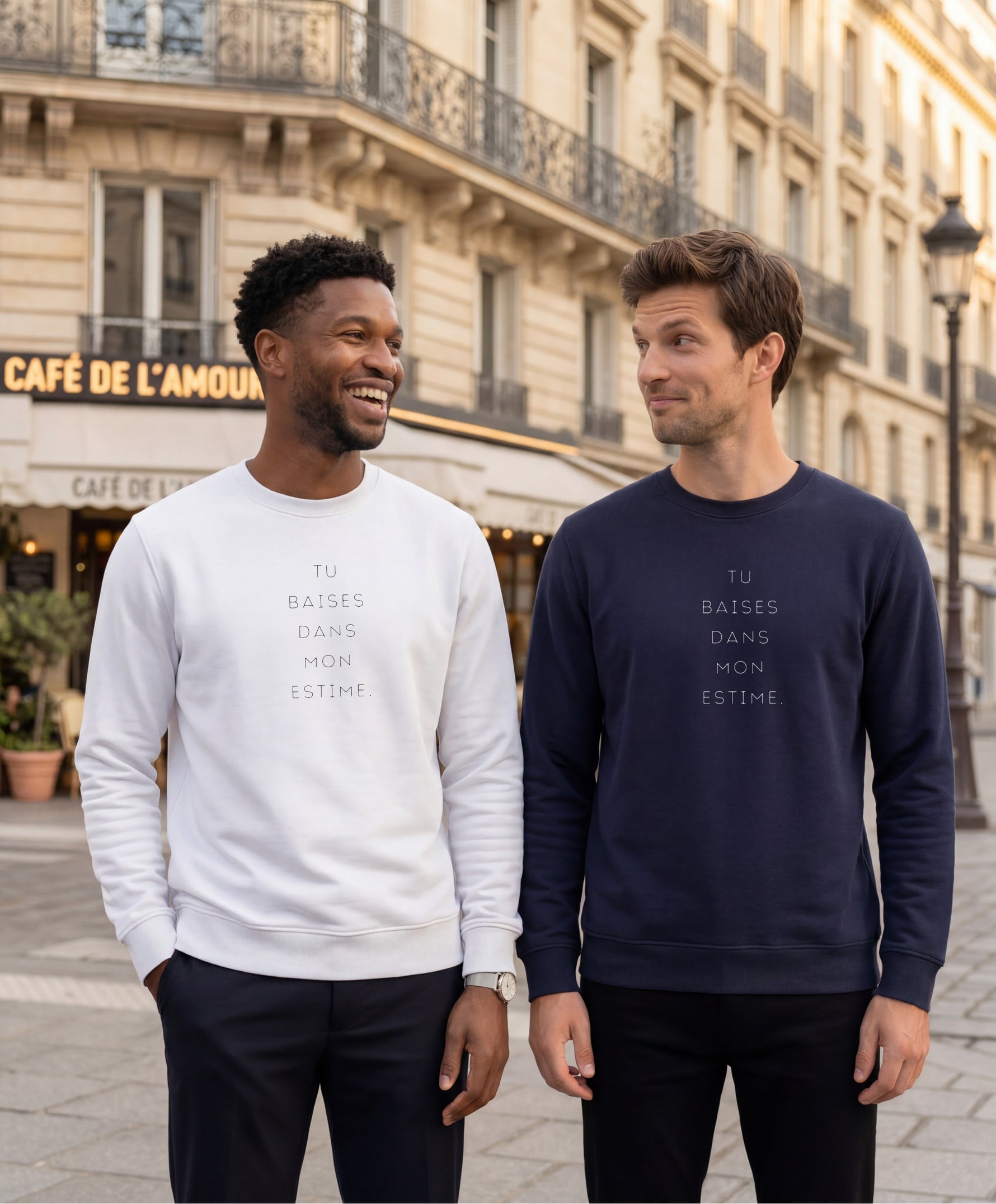 Deux hommes portant des sweatshirts Salut Fred « Tu baises dans mon estime. », l’un en blanc et l’autre en bleu marine, dans une rue parisienne devant un café parisien classique