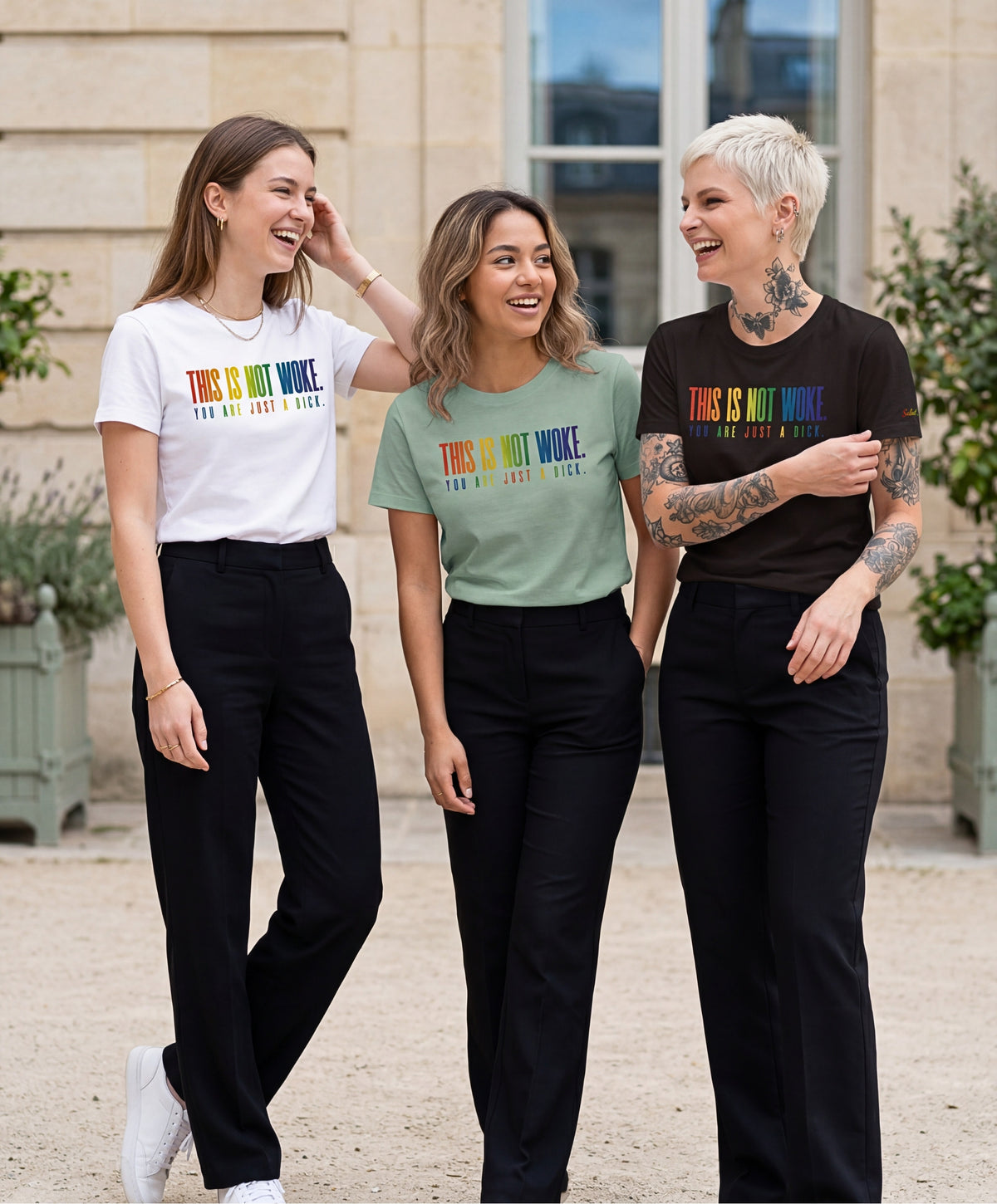Groupe de femmes portant des t-shirts classiques Salut Fred de la collection Pride « This is not woke. You are just a dick. » en blanc, bleu opalin et noir, avec slogans multicolores imprimés au centre de la poitrine dans une rue parisienne élégante