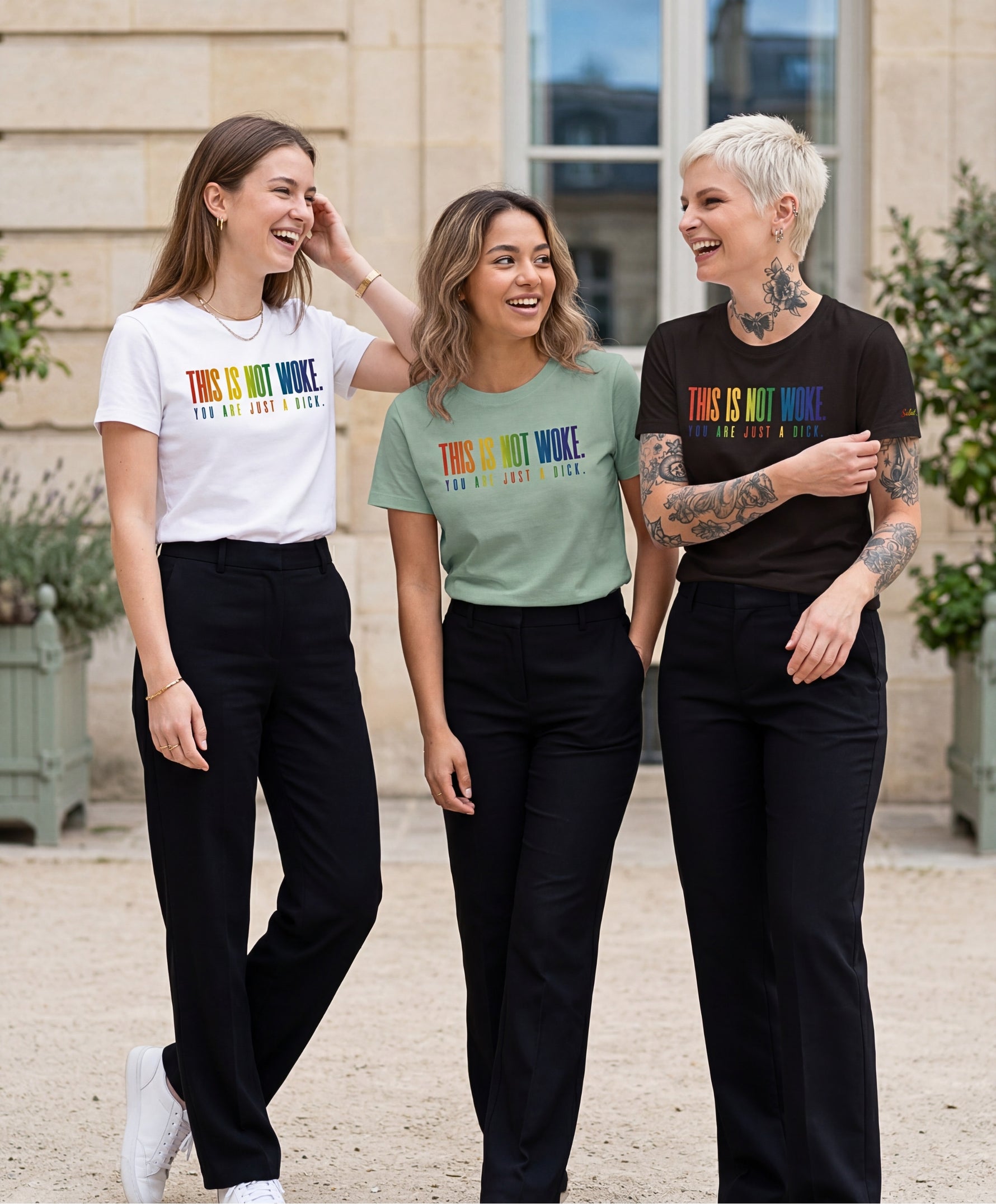 Groupe de femmes portant des t-shirts classiques Salut Fred de la collection Pride « This is not woke. You are just a dick. » en blanc, bleu opalin et noir, avec slogans multicolores imprimés au centre de la poitrine dans une rue parisienne élégante