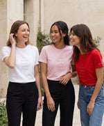 Trois femmes portant des t-shirts classiques Salut Fred blanc, rose poudré et rouge avec slogan « Tu baises dans mon estime » dans une cour parisienne lumineuse