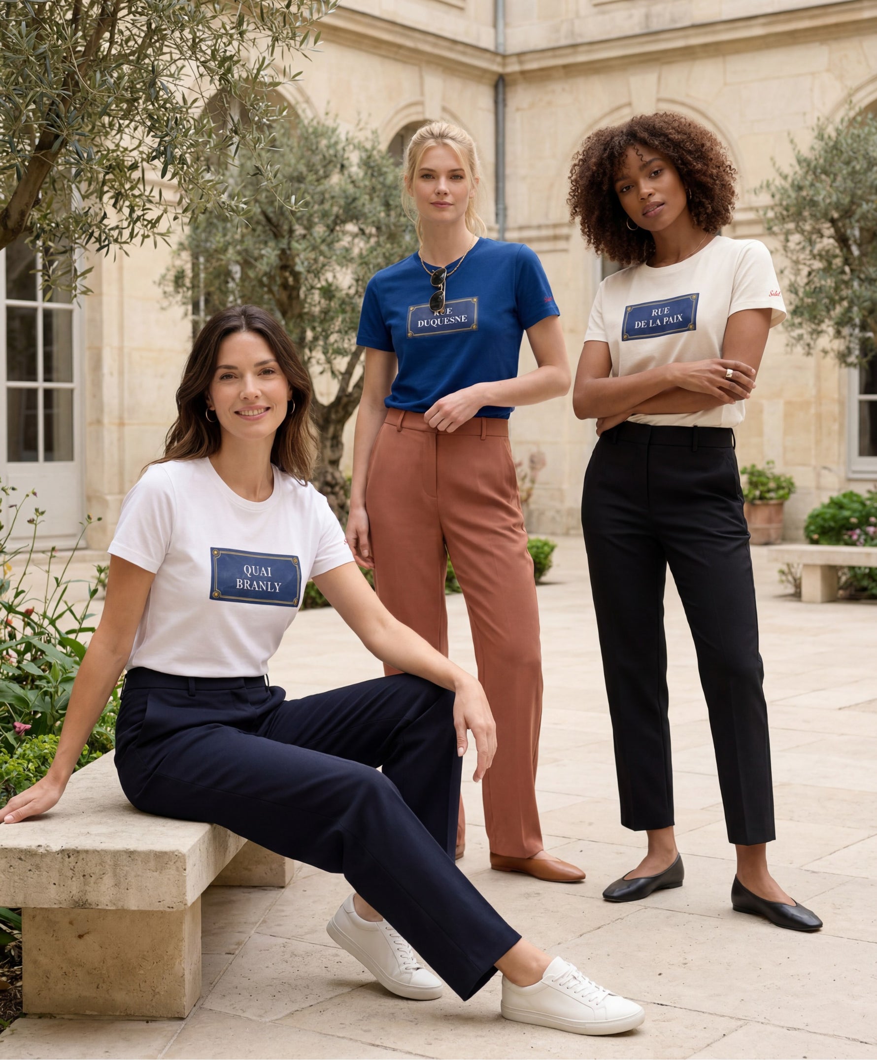 Trois femmes portant des t-shirts classiques Salut Fred blanc, écru et bleu Paris de la collection Rues de France dans une cour parisienne lumineuse