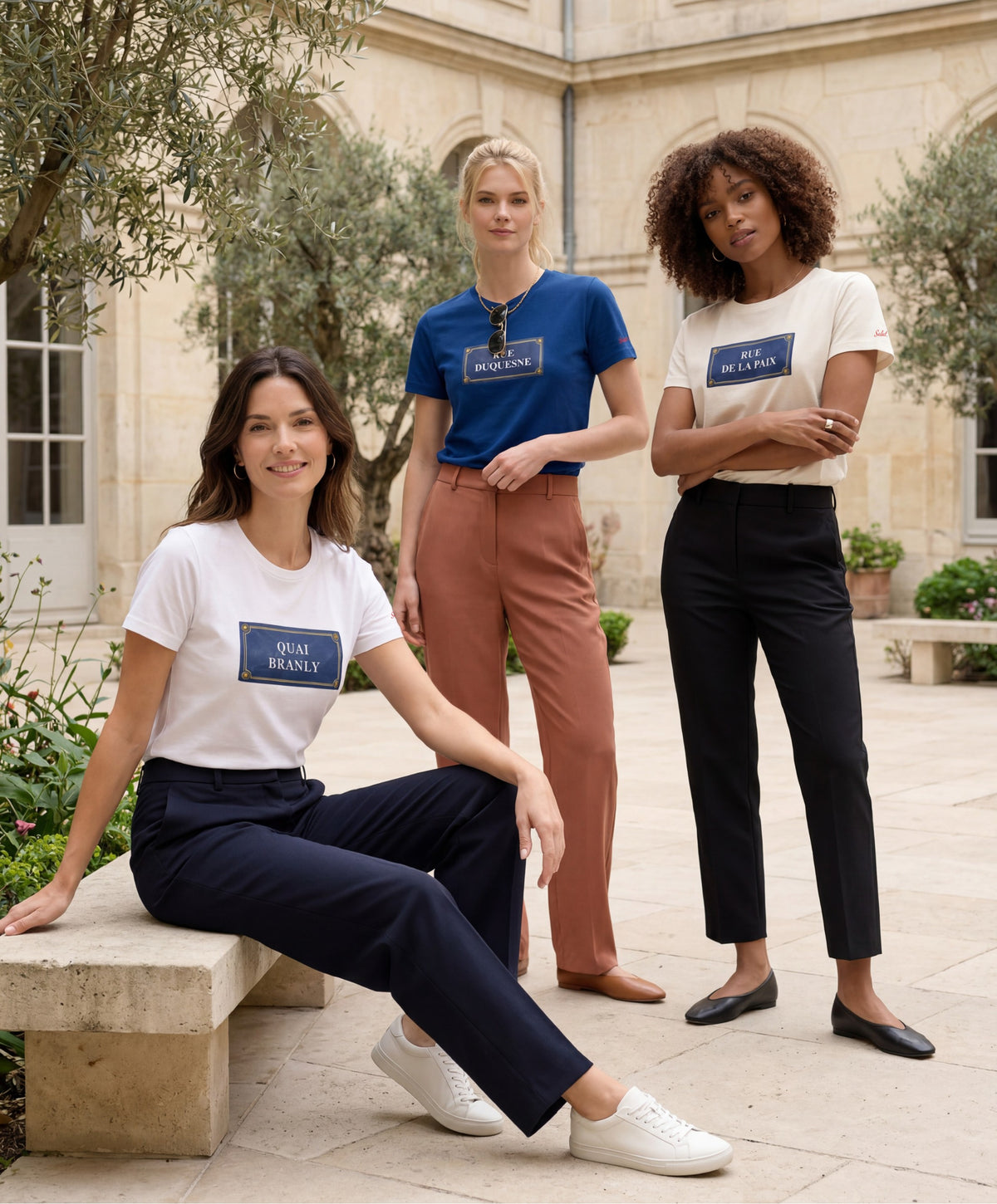 Trois femmes portant des t-shirts classiques Salut Fred blanc, écru et bleu Paris de la collection Rues de France dans une cour parisienne lumineuse