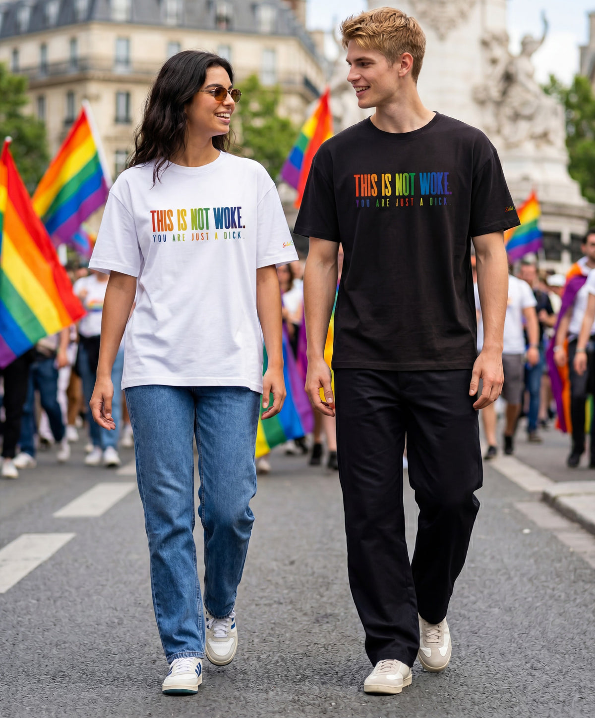 Une femme portant un t-shirt oversize blanc Salut Fred et un homme portant un t-shirt oversize noir Salut Fred de la collection Pride « This is not woke. You are just a dick. », marchant côte à côte lors d’une marche des fiertés avec slogans multicolores imprimés au centre de la poitrine