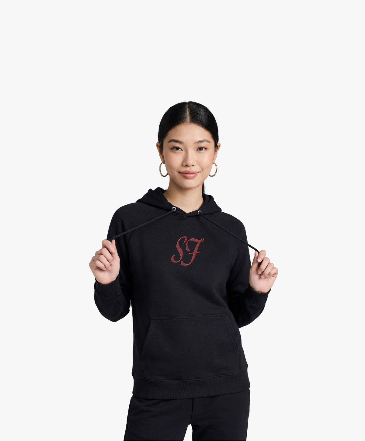 Vue de face d’une femme portant le hoodie noir Salut Fred avec monogramme SF rouge brodé au centre de la poitrine et Salut Fred brodé sur le poignet gauche