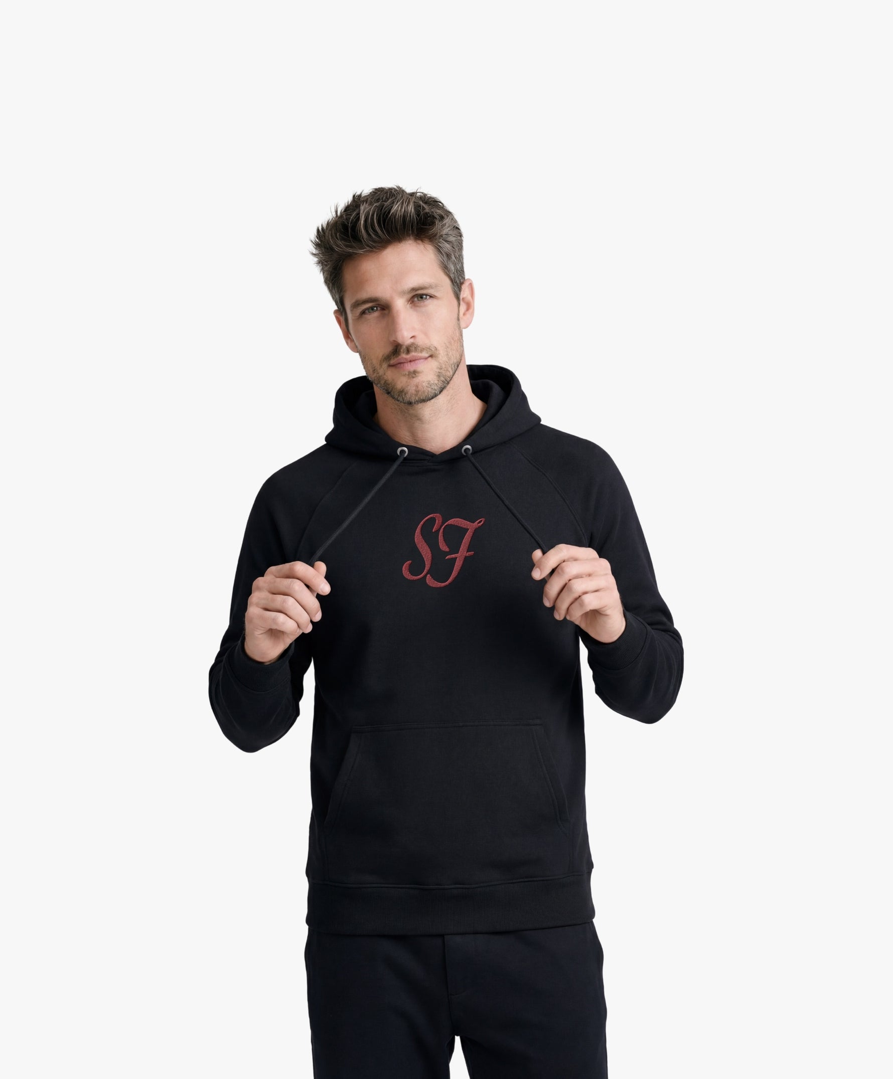 Vue de face d’un homme portant le hoodie noir Salut Fred avec monogramme SF rouge brodé au centre de la poitrine et Salut Fred brodé sur le poignet gauche
