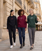 Vue de face de trois femmes portant une sélection de hoodies SF Monogramme Salut Fred en bordeaux, noir et vert profond dans une rue parisienne bordée d’immeubles haussmanniens