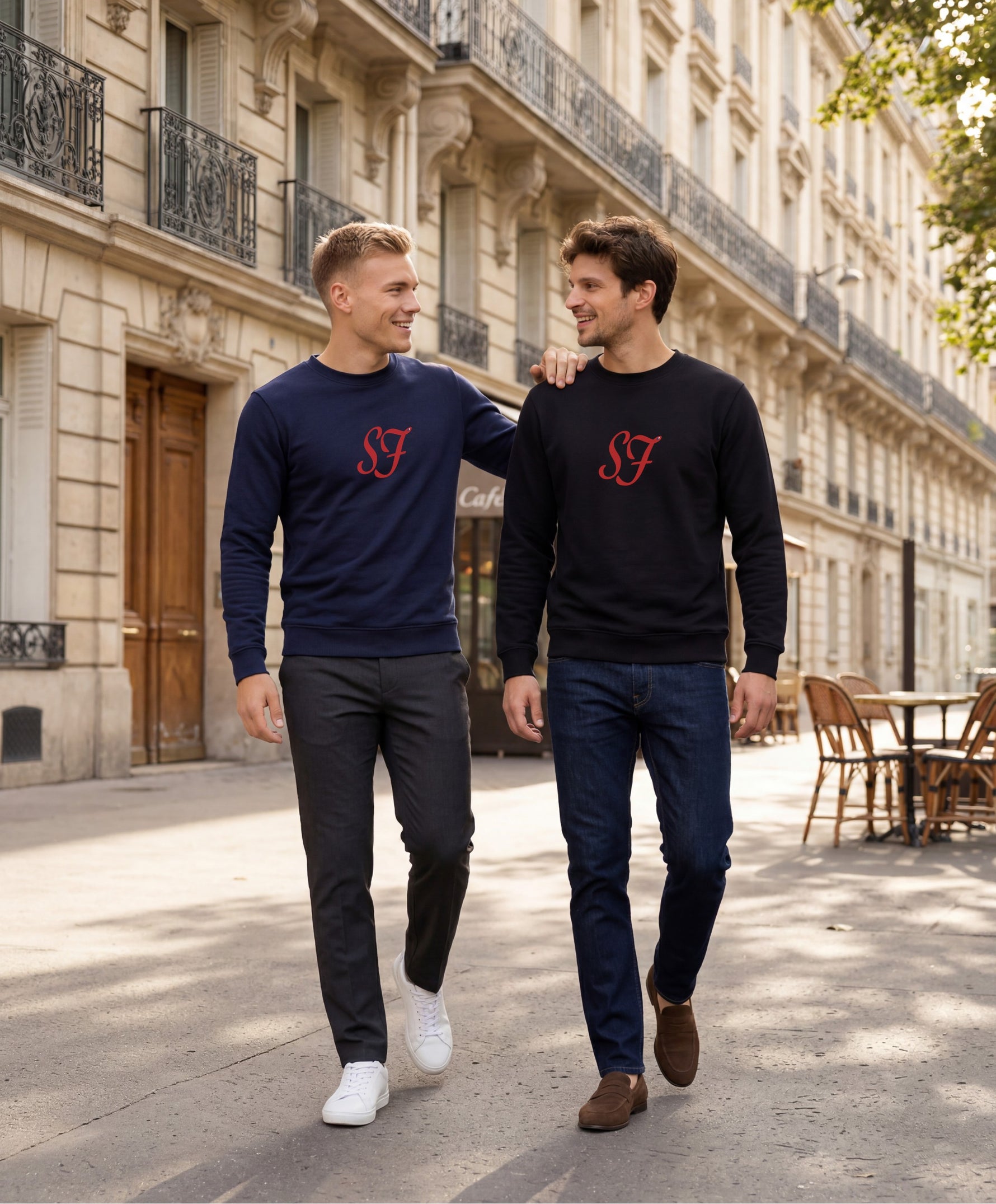 Vue de face de deux hommes portant les sweatshirts SF Monogramme Salut Fred en noir et bleu marine avec monogramme SF imprimé au centre de la poitrine dans une rue parisienne lumineuse bordée d’immeubles haussmanniens