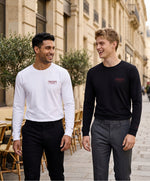 Deux hommes portant des t-shirts manches longues Salut Fred « Thérap(e)ute. À votre service » dans une rue parisienne élégante, modèle blanc et modèle noir avec motif brodé sur la poitrine gauche et logo Salut Fred brodé sur le poignet gauche