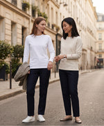 Deux femmes portant des t-shirts à manches longues Salut Fred blanc et écru avec broderie rouge sur le poignet gauche, dans une rue parisienne aux façades haussmanniennes élégantes.
