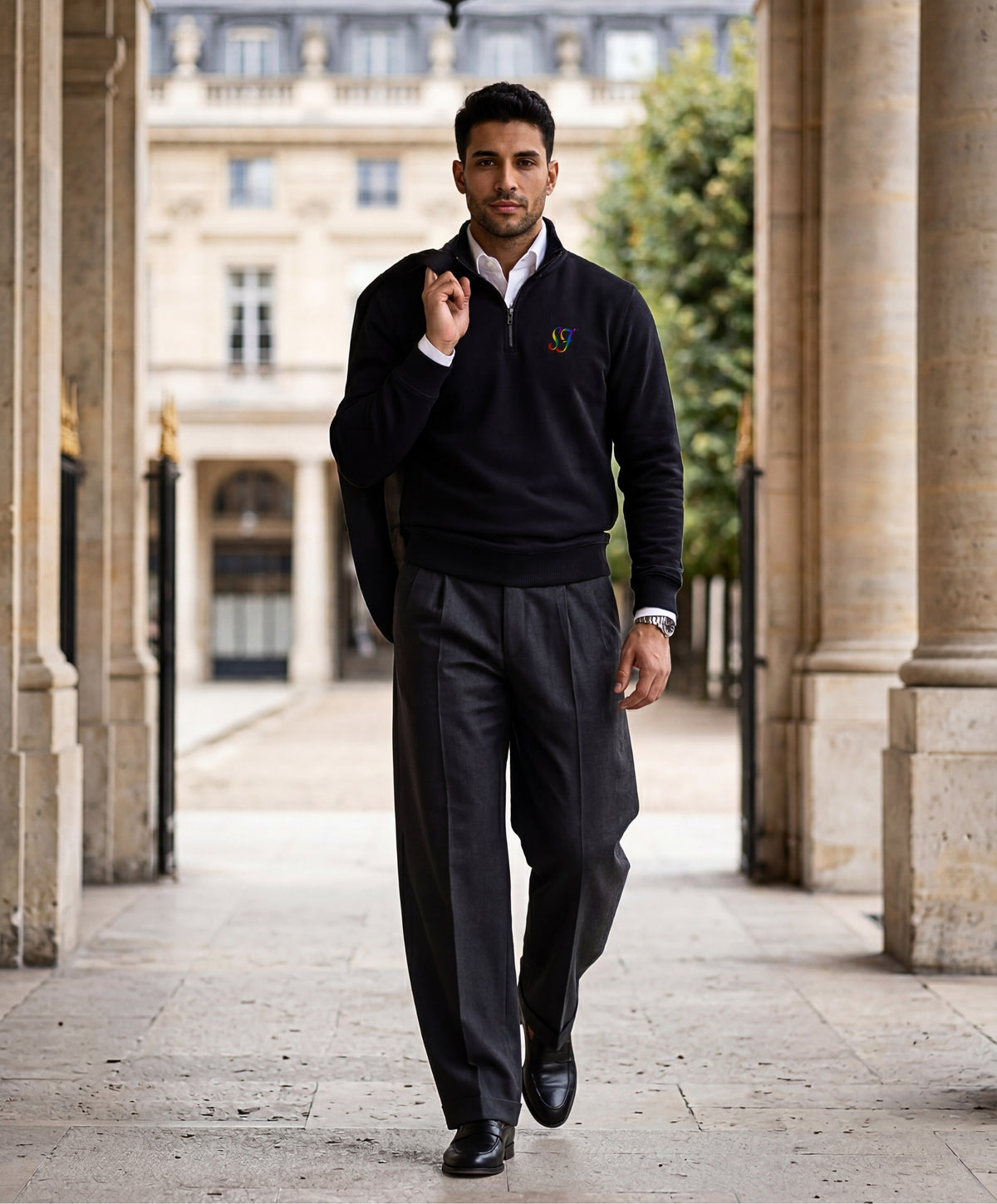 Vue de face d’un homme portant un sweatshirt à col zippé 1/4 noir Salut Fred de la collection Pride avec monogramme SF arc-en-ciel brodé sur la poitrine, dans une galerie parisienne élégante