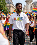 Vue de face d’un homme portant un t-shirt oversize blanc Salut Fred de la collection « This is not woke. You are just a dick. » lors d’une marche Pride, avec slogan multicolore imprimé au centre de la poitrine et logo Salut Fred arc-en-ciel sur la manche gauche