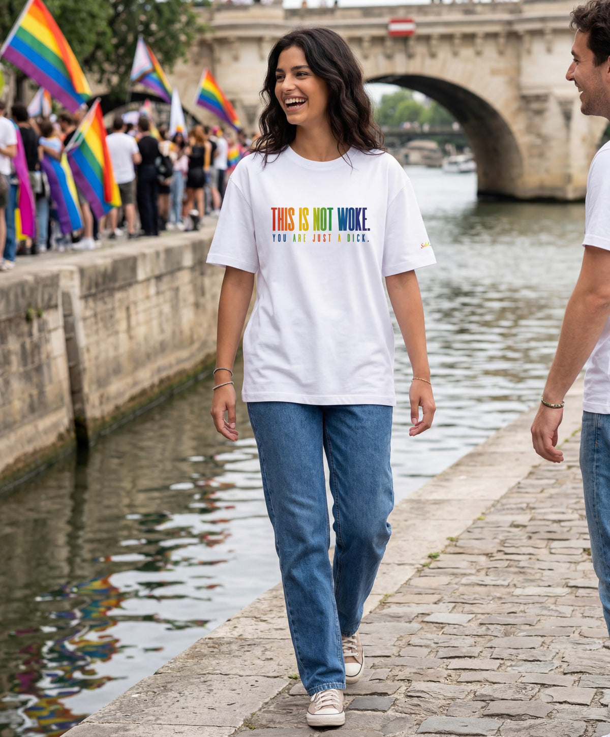 Vue de face d’un homme portant un t-shirt oversize blanc Salut Fred de la collection « This is not woke. You are just a dick. » lors d’une marche Pride, avec slogan multicolore imprimé au centre de la poitrine et logo Salut Fred arc-en-ciel sur la manche gauche