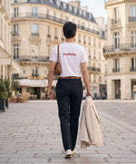 Vue de dos d’une femme portant un t-shirt classique blanc Salut Fred avec melèche imprimé au haut du dos dans une teinte melon pastel saumonée, pantalon noir ajusté, blazer écru à la main et sac en cuir camel dans une place parisienne élégante