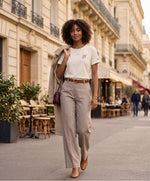 Vue de face d’une femme portant un t-shirt classique écru Salut Fred avec monogramme SF brodé sur la poitrine gauche, broderie Salut Fred sur la manche gauche, pantalon beige fluide, ceinture camel et bottines camel dans une rue parisienne élégante