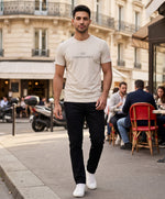Vue de face d’un homme portant le t-shirt classique écru « Zizi l’Impératrice » avec texte imprimé noir centré sur la poitrine et logo Salut Fred sur la manche gauche, dans une rue parisienne en terrasse.