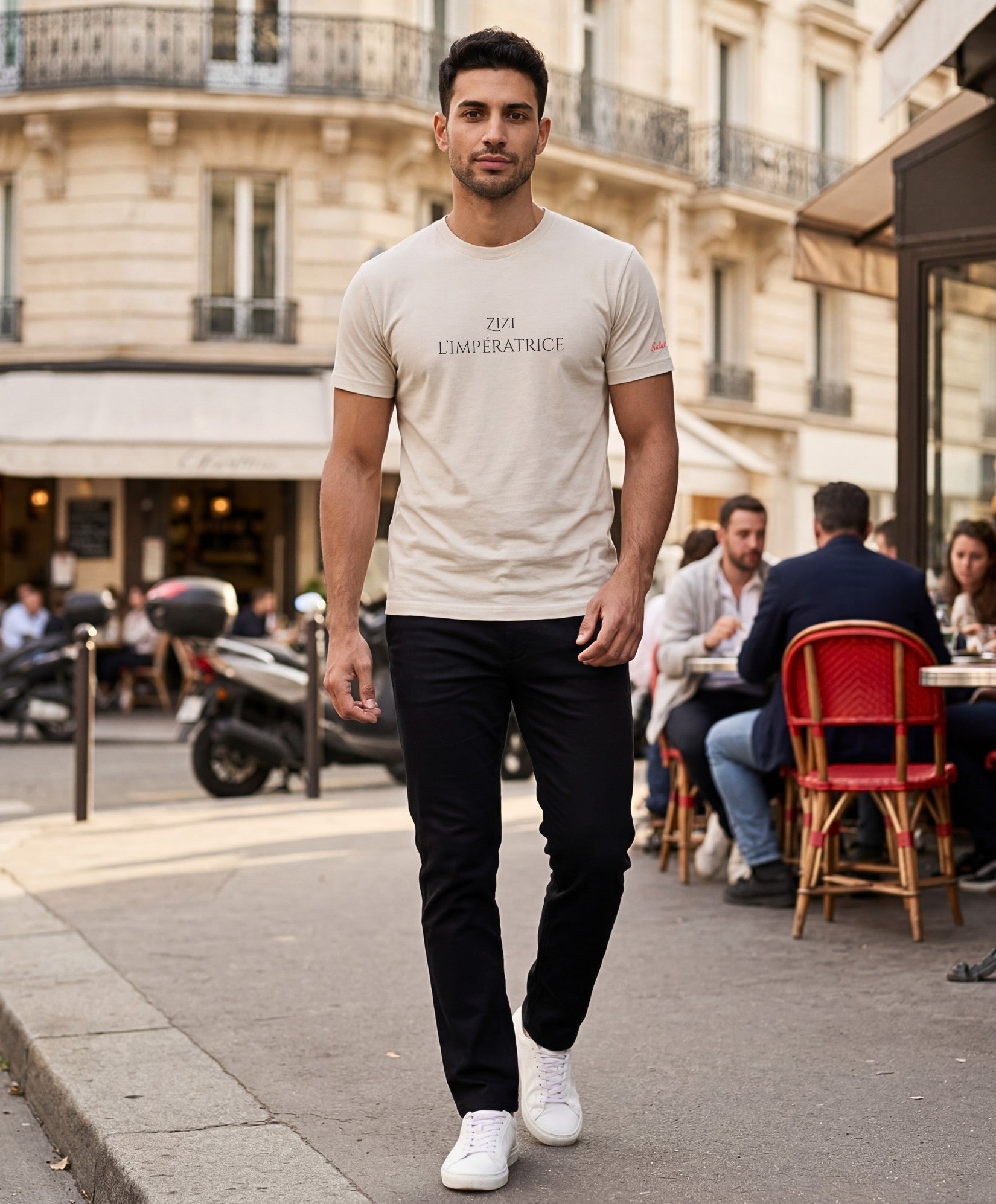 Vue de face d’un homme portant le t-shirt classique écru « Zizi l’Impératrice » avec texte imprimé noir centré sur la poitrine et logo Salut Fred sur la manche gauche, dans une rue parisienne en terrasse.