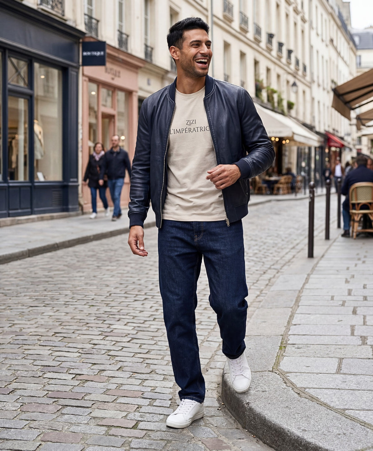 Vue de face d’un homme portant le t-shirt classique écru « Zizi l’Impératrice » avec texte imprimé noir centré sur la poitrine et logo Salut Fred sur la manche gauche, associé à un blouson en cuir bleu marine dans une rue parisienne pavée.