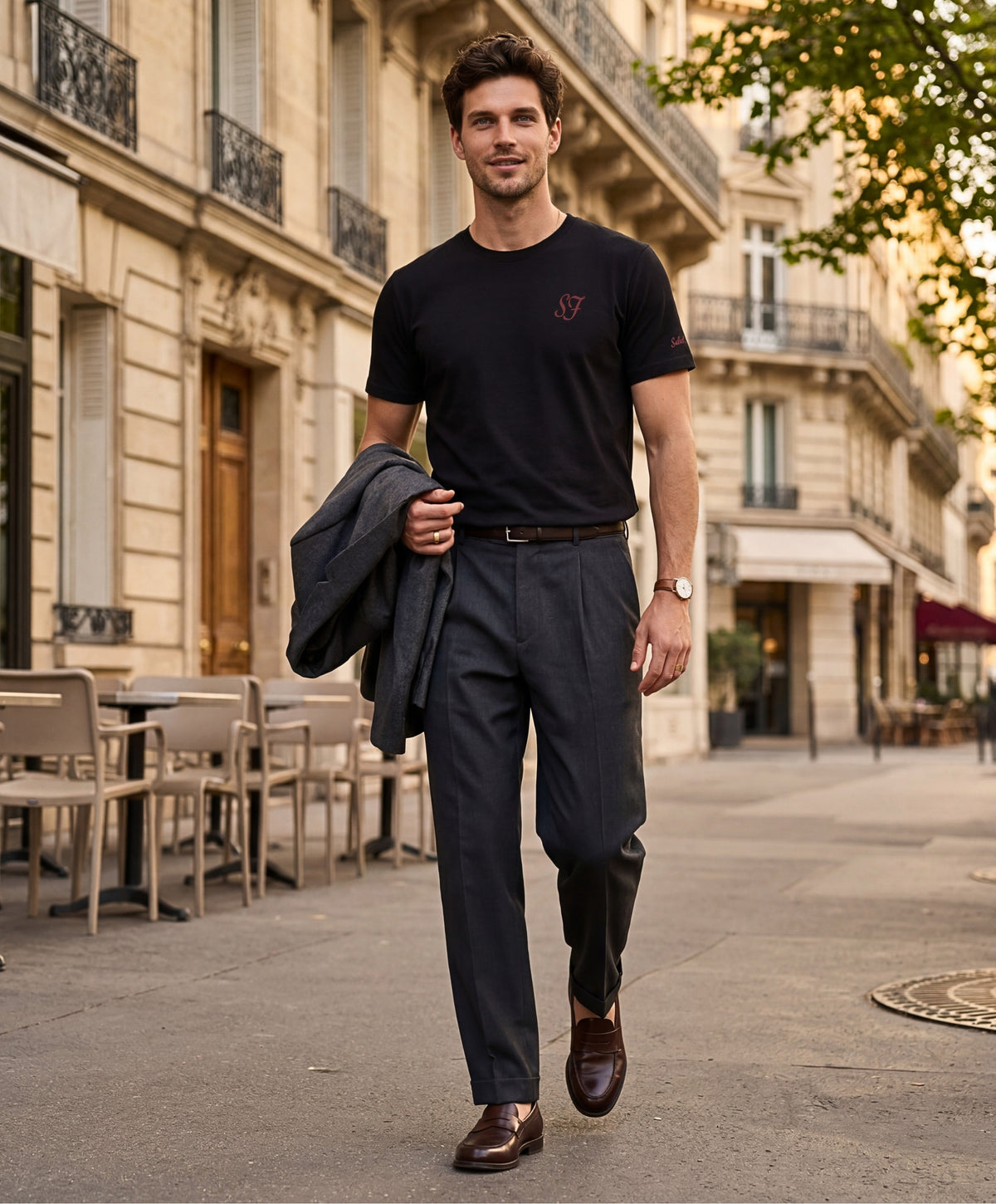 Vue de face d’un homme portant un t-shirt classique noir Salut Fred avec monogramme SF brodé sur la poitrine gauche et broderie Salut Fred sur la manche gauche, pantalon gris graphite habillé, mocassins marron et veste gris graphite dans une rue parisienne élégante