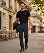 Vue de face d’un homme portant un t-shirt classique noir Salut Fred avec monogramme SF brodé sur la poitrine gauche et broderie Salut Fred sur la manche gauche, pantalon gris graphite habillé, mocassins marron et veste gris graphite dans une rue parisienne élégante