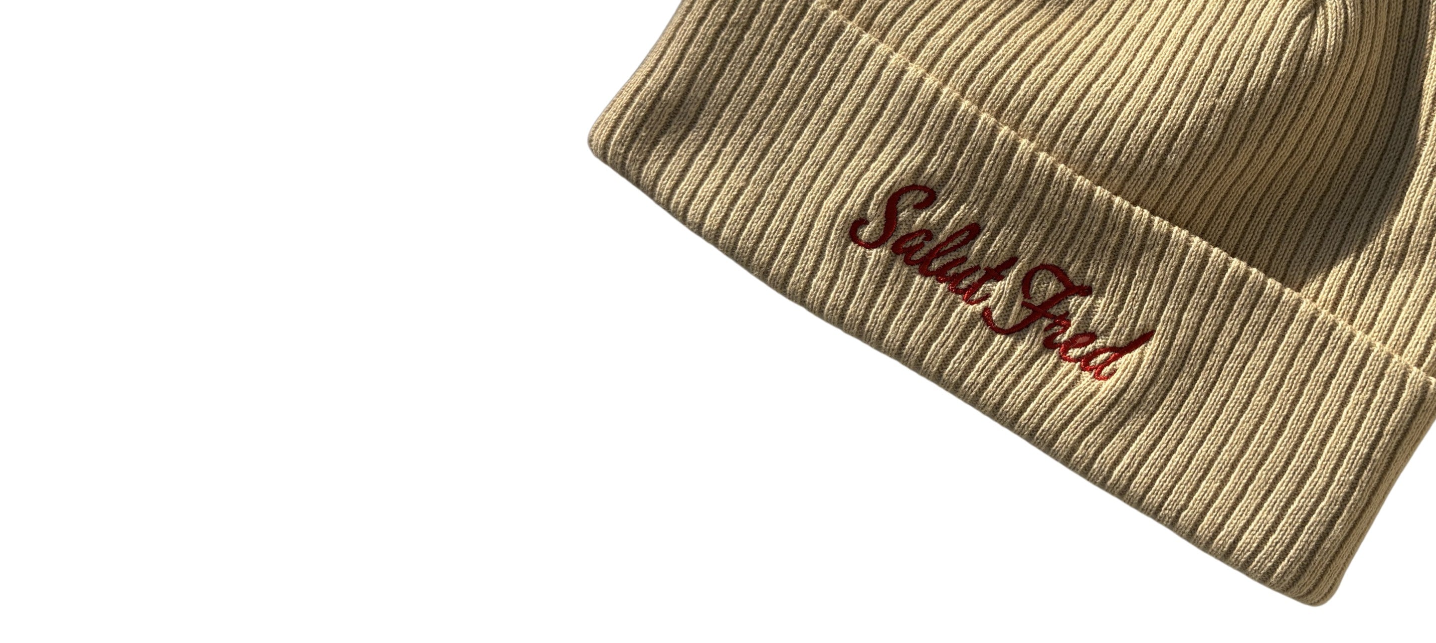 Détail de la broderie rouge Salut Fred sur un bonnet beige en coton bio à maille côtelée avec large revers.
