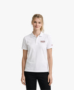 Vue de face d’une femme portant un polo blanc Salut Fred avec broderie « Thérap(e)ute. À votre service » sur la poitrine et Salut Fred brodé sur la manche gauche dans une rue parisienne élégante