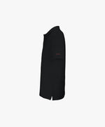 Vue côté gauche du polo noir Salut Fred avec broderie « Thérap(e)ute. À votre service », avec Salut Fred brodé près de l’épaule gauche