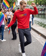 Vue de face d’un homme portant un sweatshirt rouge Salut Fred de la collection « This is not woke. You are just a dick. » avec slogan multicolore imprimé au centre de la poitrine, lors d’une Pride parisienne festive