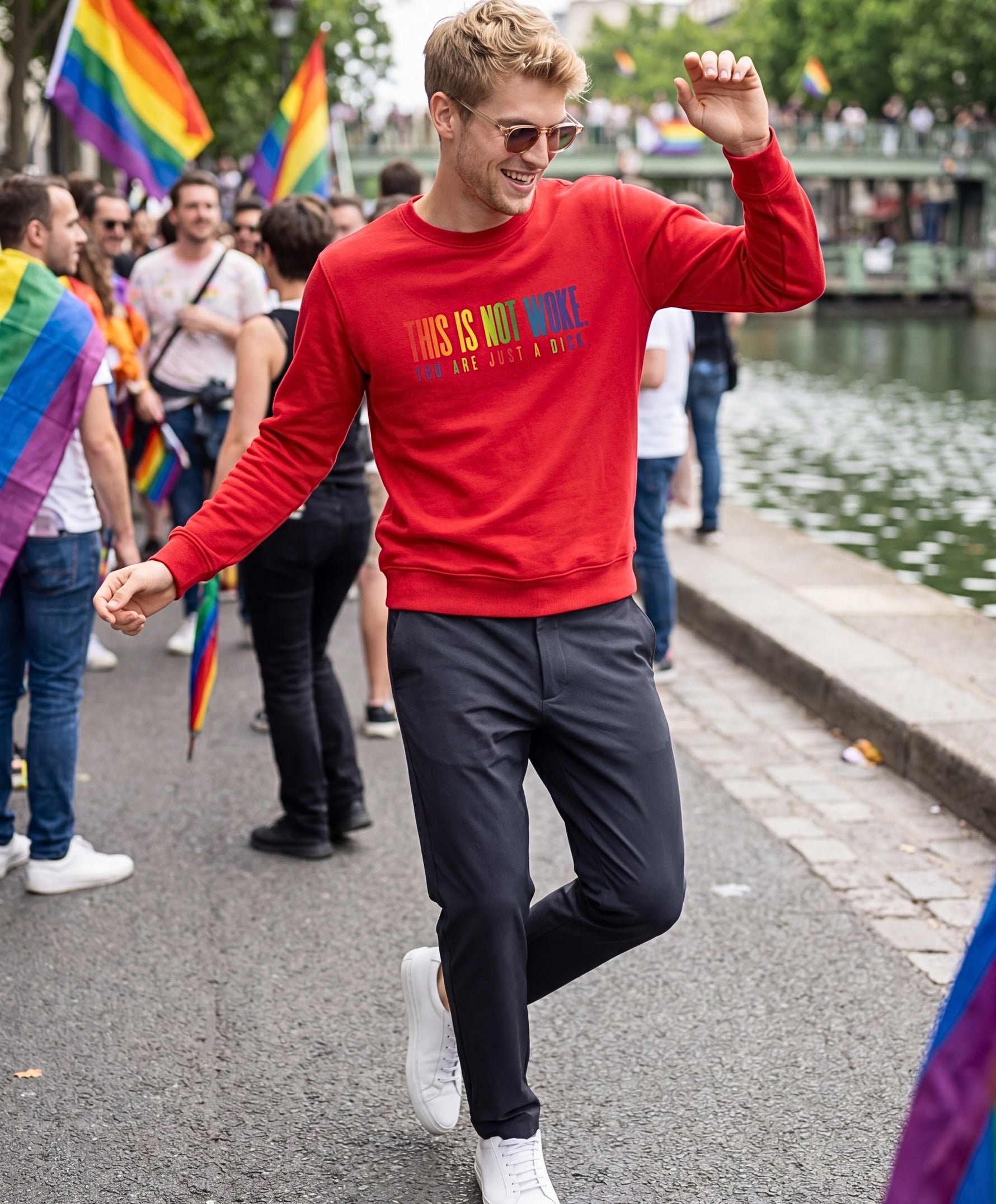 Vue de face d’un homme portant un sweatshirt rouge Salut Fred de la collection « This is not woke. You are just a dick. » avec slogan multicolore imprimé au centre de la poitrine, lors d’une Pride parisienne festive