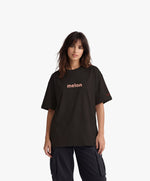 Femme vue de face portant le t-shirt oversize noir « Melon Melèche » avec texte imprimé « melon » centré sur la poitrine et logo Salut Fred sur la manche gauche.