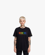 Vue de face d’une femme portant un t-shirt oversize noir Salut Fred de la collection « This is not woke. You are just a dick. » avec slogan multicolore imprimé au centre de la poitrine et logo Salut Fred arc-en-ciel sur la manche gauche