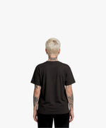 Vue de dos d’une femme portant un t-shirt oversize noir Salut Fred de la collection « This is not woke. You are just a dick. »